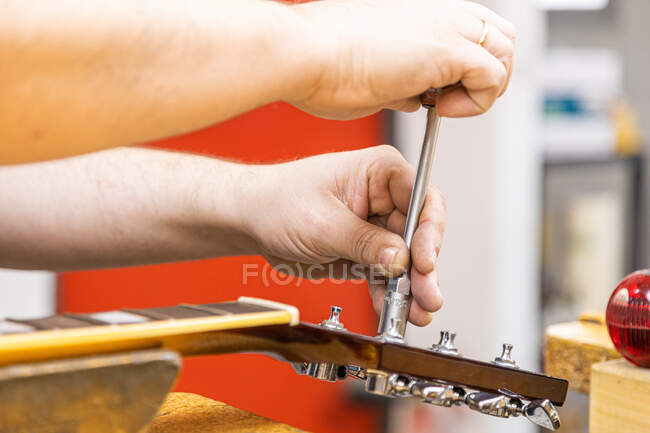 Crop unrecognizable craftsman using tubular socket wrench while repairing guitar in professional workshop — Stock Photo