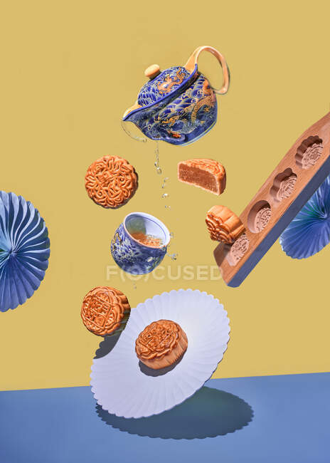 Xícara e bule de chá com chá caindo com bolos tradicionais doces chineses e moldes de cozimento na mesa azul contra fundo amarelo — Fotografia de Stock