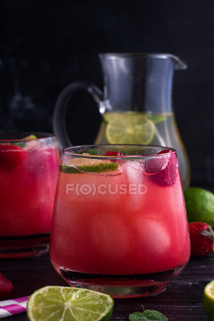 Glasses of cold coconut water with lime slices and strawberries served on dark wooden table — Stock Photo