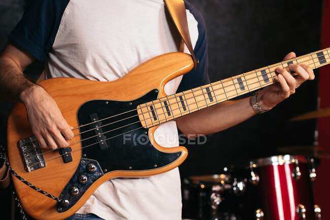 Обрезанный неузнаваемый мужчина в повседневной одежде играет на бас-гитаре в легком клубе — стоковое фото