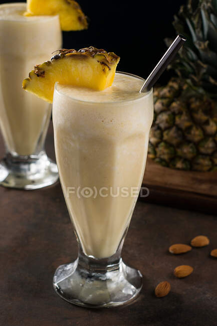 Sweet refreshing cold pina colada smoothie served with pineapple slices on table with scattered almond — Stock Photo