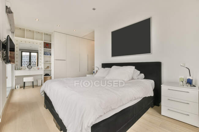 Comodo letto con lenzuola bianche posizionato vicino al comodino in spaziosa camera da letto con TV e porta a vetri in elegante appartamento — Foto stock