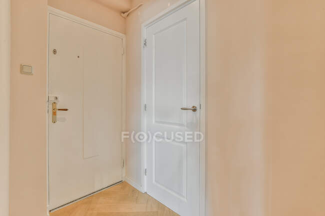 White doors with metal handles between beige walls with switch and shades in passage with parquet — Stock Photo