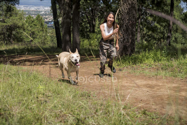 Corpo pieno di proprietaria attiva che corre su strada rurale con cane leale mentre si allena nel boschetto nella giornata estiva — Foto stock