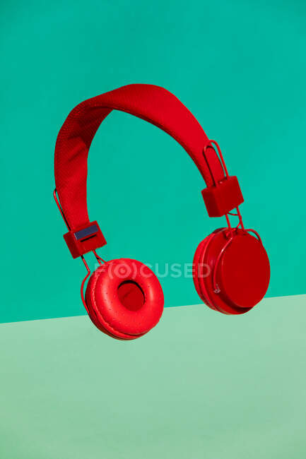 Cuffie rosse moderne senza fili per l'ascolto di musica appese in aria su sfondo verde brillante — Foto stock