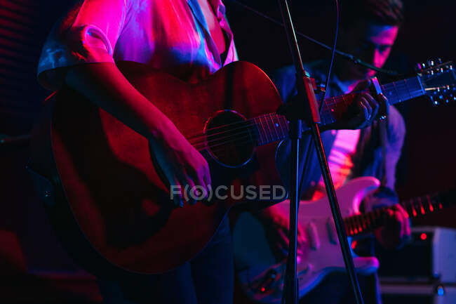 Homem tocando guitarra enquanto mulher cantando e cantando música no clube com luzes de néon — Fotografia de Stock