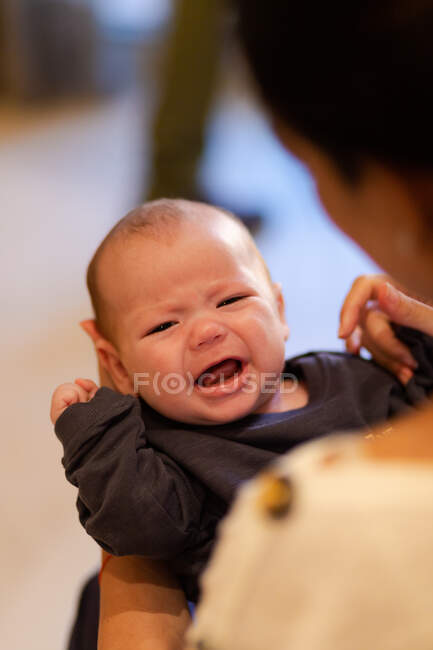 Cortar mãe irreconhecível abraçando adorável recém-nascido chorando e olhando para a câmera à luz do dia — Fotografia de Stock