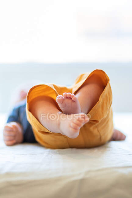 Анонімний милий босоніж дитина лежить на самоті на зручному ліжку в сонячний ранок вдома — стокове фото