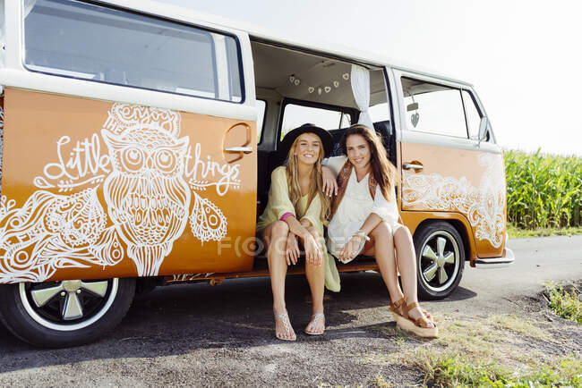 Две симпатичные девушки в летней одежде сидят на полу фургона и смотрят в камеру. — стоковое фото
