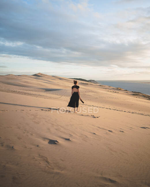 Full body back view of unrecognizable barefoot female in dress strolling at sunset on sandy dune in desert — Stock Photo