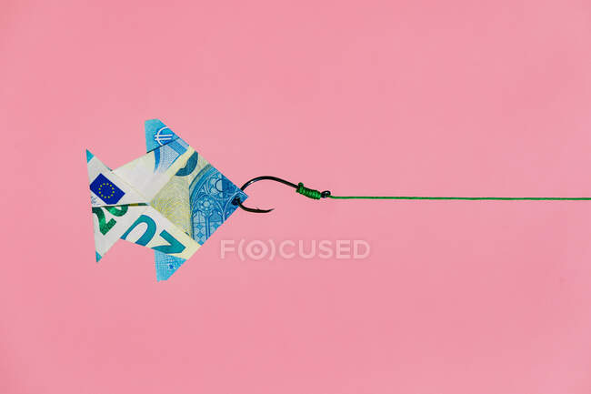 Gancho en línea tirando de origami peces en forma de billete en euros como concepto de riqueza y dinero que gana contra el fondo rosa - foto de stock