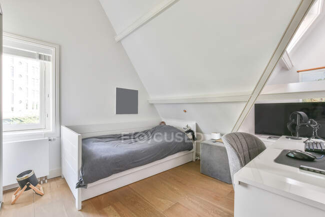 Interior of kid bedroom with comfortable bed and computer placed on working desk in attic of light house — Stock Photo