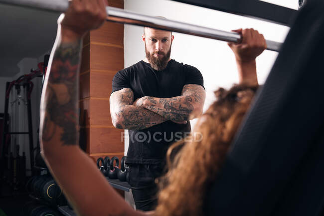 Deportista fuerte concentrado levantando pesas pesadas con pesas durante el entrenamiento funcional con instructor en gimnasio - foto de stock