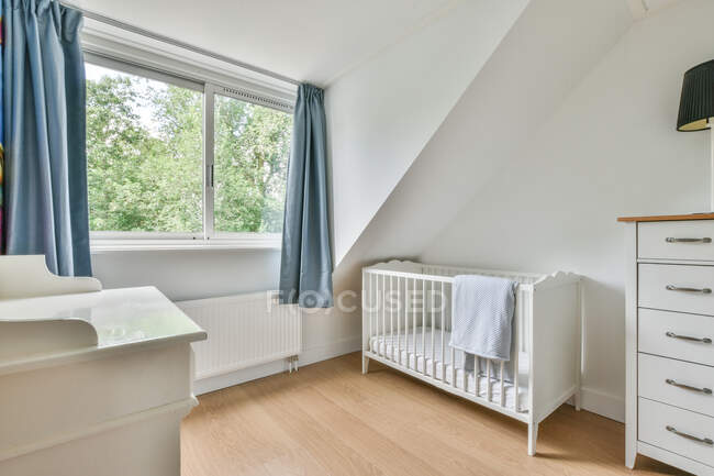 Weißes Kinderbett mit Handtuch im hellen, stilvollen Schlafzimmer mit Lampe auf der Kommode — Stockfoto