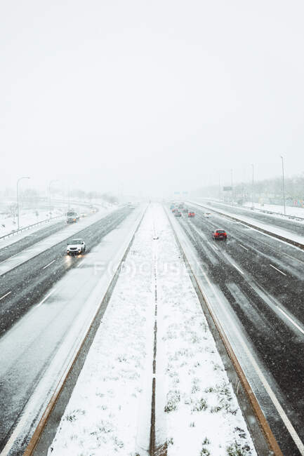Cars driving on smooth asphalt roadway covered with snow in gloomy winter day during snowfall in Madrid — Stock Photo