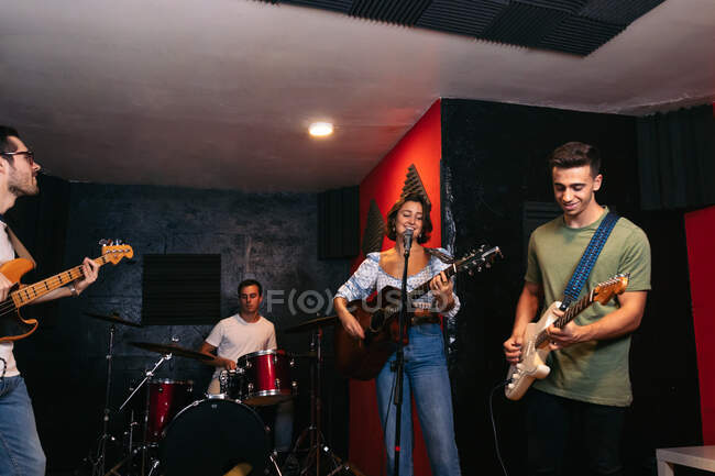 Grupo de personas en ropa casual tocando guitarras y tambores mientras mujer cantando y cantando canción en el club - foto de stock