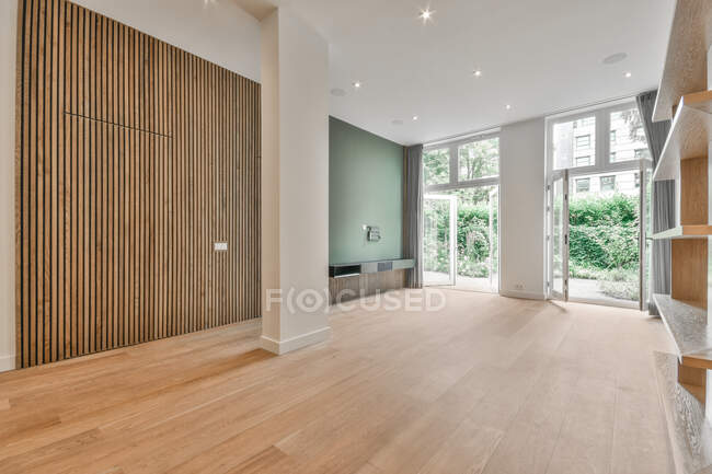 Interior of minimalist styled apartment with wooden floor and empty shelves near opened doors leading to winter garden — Stock Photo