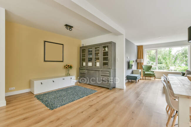 Armadio grigio posto a parete con mazzo di fiori in luminoso soggiorno con sedie a tavola in elegante appartamento con finestra — Foto stock