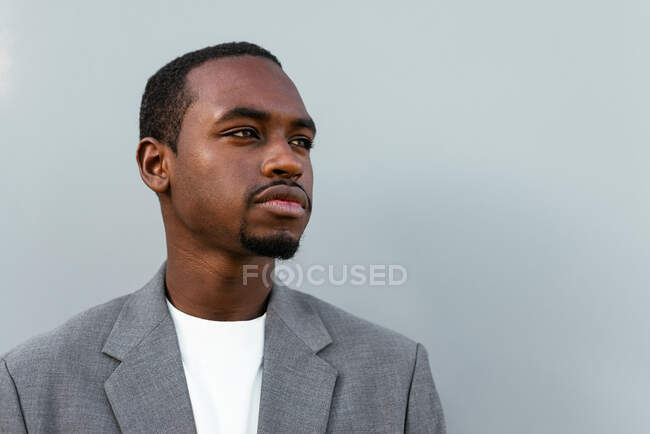 Seriöser afroamerikanischer Unternehmer im formellen Anzug steht vor grauem Hintergrund und schaut weg — Stockfoto