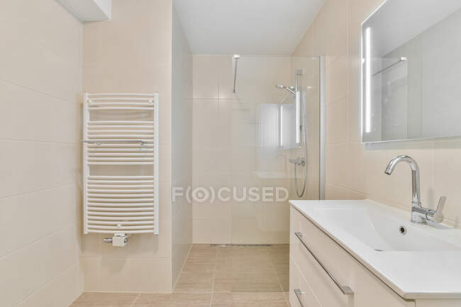 Design criativo do banheiro com toalheiro aquecido contra lavatório com torneira sob espelho em casa de luz — Fotografia de Stock