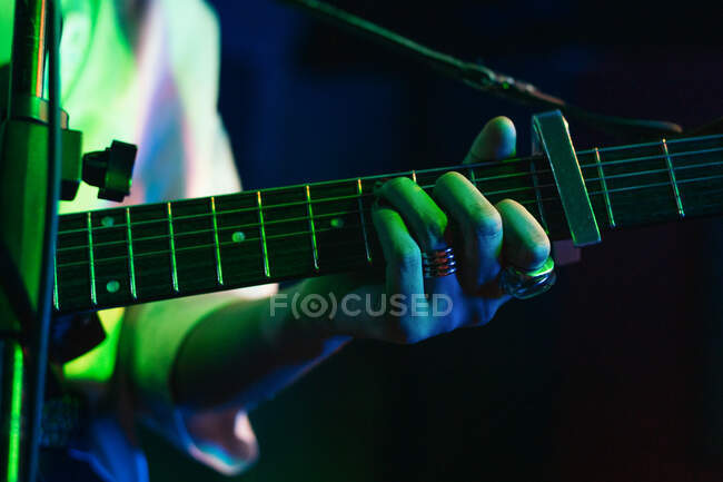 Guitarrista femenina irreconocible recortada tocando la guitarra acústica en el club de luz - foto de stock