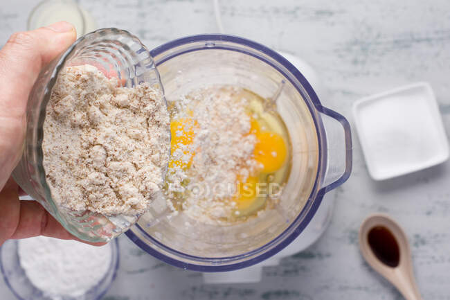 Верхній вигляд врожаю Анонімний самець заливає здорове мигдалеве борошно в блендер з яйцями під час приготування шипшини на кухні. — стокове фото