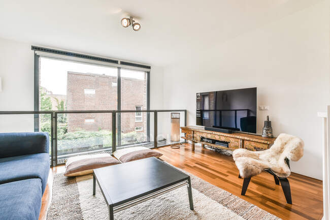 Bequemes Sofa neben Tisch auf Teppich gegen Wand mit modernem Fernseher im Wohnzimmer mit Fenster und stilvollem Interieur — Stockfoto