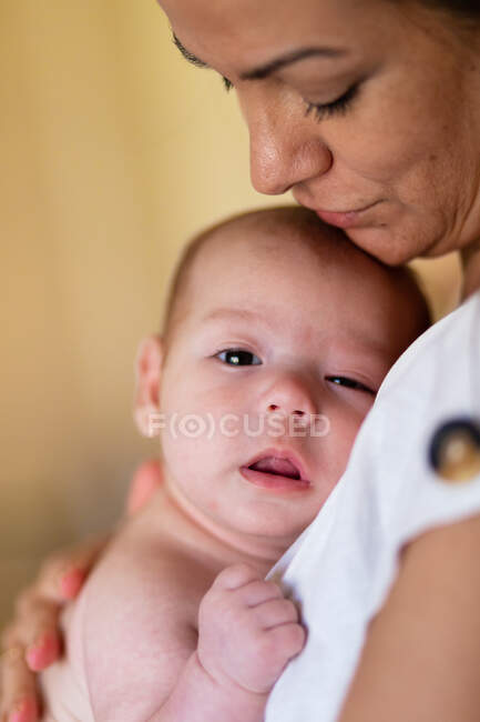 Vista lateral de la cosecha tranquila mujer joven abrazando y acariciando adorable bebé en el día - foto de stock