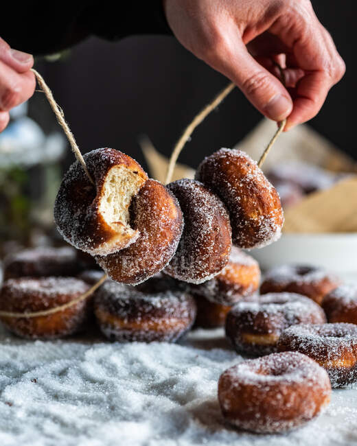 Crop unrecognizable female holding tasty lent donuts in sugar powder on thread at table — Stock Photo