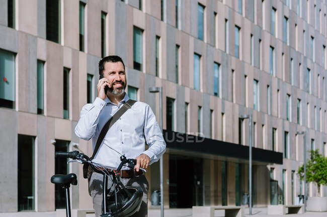 Мужчина в формальной одежде стоит с велосипедом и разговаривает по мобильному телефону в центре города — стоковое фото