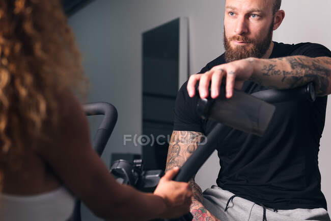Culturista muscoloso fiducioso con tatuaggi che parlano contro lo sportivo anonimo in palestra durante il giorno — Foto stock