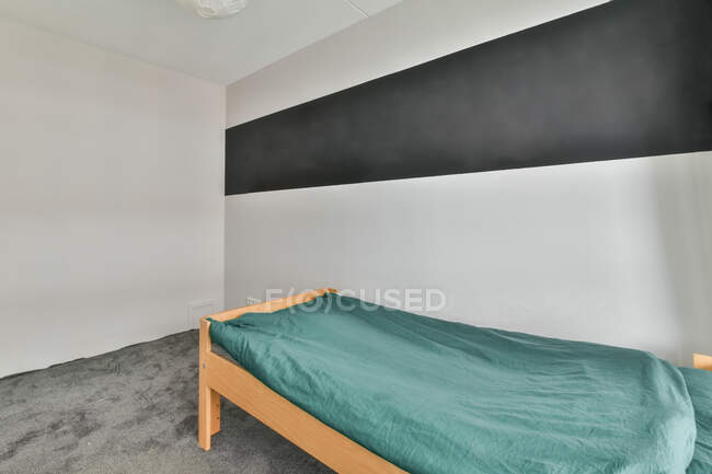 Innengestaltung des Schlafzimmers mit heller Wand und grauem Boden und Einzelbett mit türkisfarbener Decke — Stockfoto