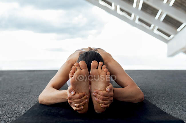 Nicht wiederzuerkennende, flexible Barfußweibchen praktizieren Paschimottanasana-Haltung während eines Yoga-Trainings in der Nähe von Solarzellen auf der Straße in Barcelona — Stockfoto