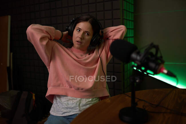 Young female radio host in casual clothes and headphones resting while recording podcast in dark studio — Stock Photo