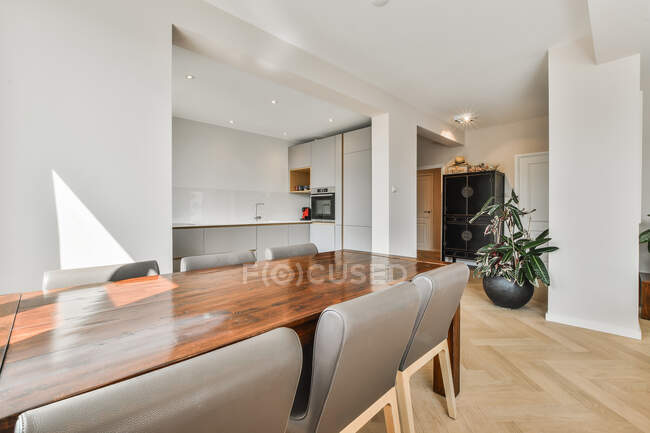 Moderno comedor y cocina interior con mesa y sillas contra macetas y horno incorporado en la casa - foto de stock