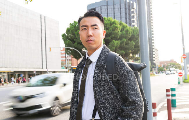 Самовпевнений молодий азіатський підприємець у стильному одязі, який дивиться убік у сонячному місті — стокове фото