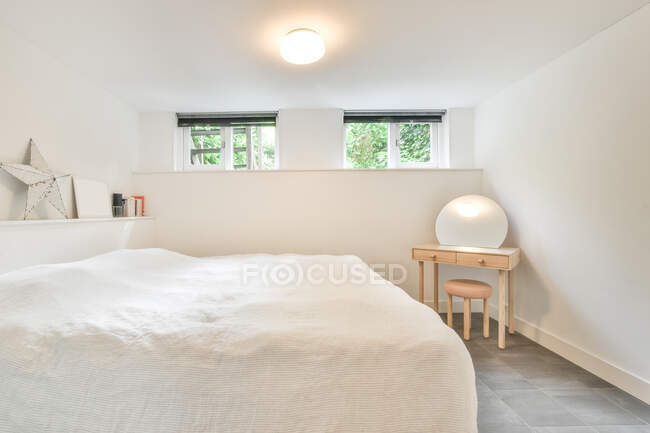 Minimalistisches Interieur eines hellen Schlafzimmers mit bequemem Bett und Tisch mit Stuhl in der Nähe von Fenstern im Tageslicht — Stockfoto