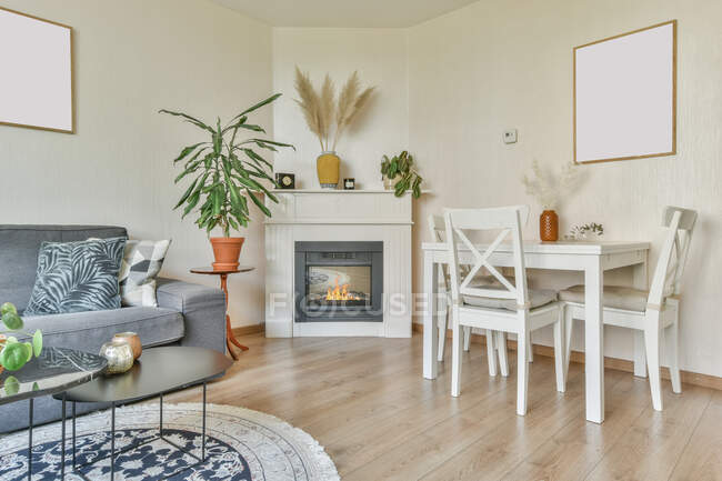 Interior de la elegante sala de estar con chimenea eléctrica decorada con florero de ramas secas cerca de sillas en la mesa y el sofá - foto de stock