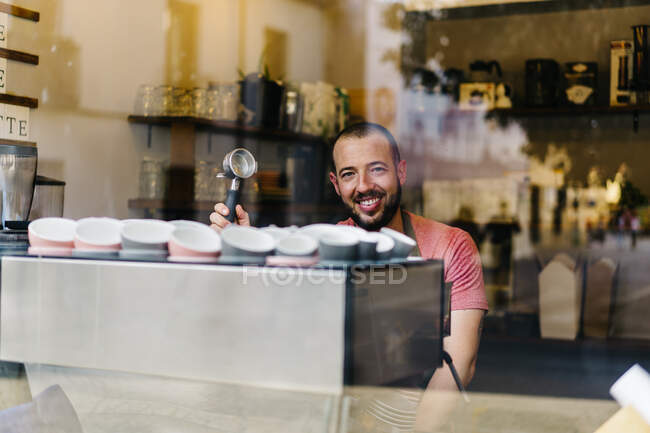 Through glass of male worker in apron preparing coffee while standing near window during work in modern cafeteria — Stock Photo