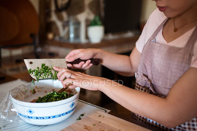 Зверху врожаю невпізнавана жінка нарізає свіжі зелені трави на дерев'яній обробній дошці, готуючи вечерю на кухні — стокове фото