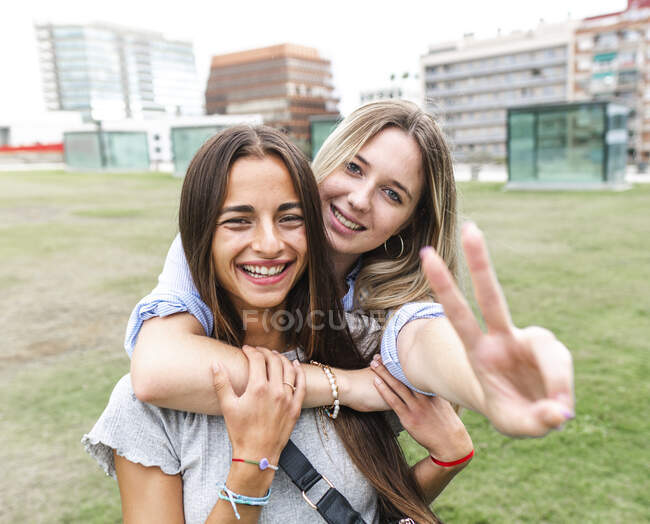 Веселі друзі-жінки посміхаються і дивляться на камеру, розважаючись на зеленій траві у дворі — стокове фото