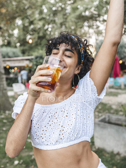 Hembra étnica positiva bebiendo refrescante cóctel y bailando mientras disfruta de la fiesta en el jardín de verano - foto de stock
