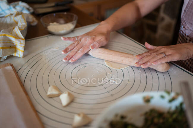 From above of crop anonymous woman in apron rolling dough on table while preparing dumplings with meat in kitchen — Stock Photo