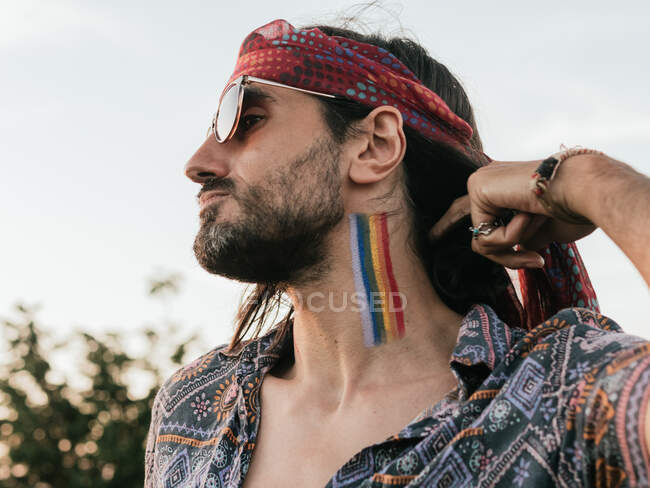 Vista lateral de un hombre sin emociones con bandera lgtbi pintada en su cuello. - foto de stock