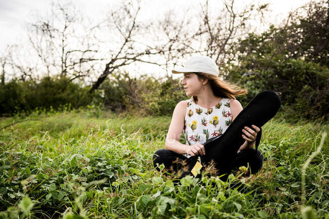 Calma musicista donna in abiti casual seduta su erba verde e apertura cassa nera di ukulele acustico alla luce del giorno — Foto stock