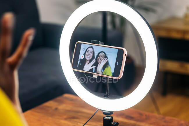 Crop anonymous person using modern smartphone with illuminating ring lamp on tripod for calling friends — Stock Photo