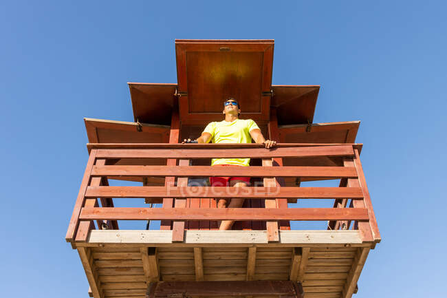 Dal basso bagnino maschio che controlla la sicurezza in mare dalla torre di salvataggio in legno — Foto stock