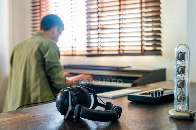 Selective focus of headphones placed on wooden table against male musician playing piano near window — Stock Photo