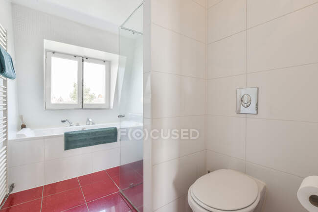 Современный санузел с унитазом против ванны и окна в доме с кафельным полом — стоковое фото