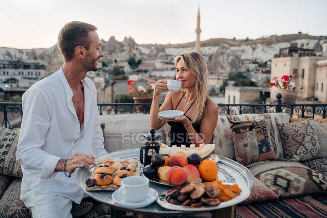 Content loving man and woman drinking tea and looking at each other while spending time together on terrace of cafe with pillows in Turkey Cappadocia — Stock Photo